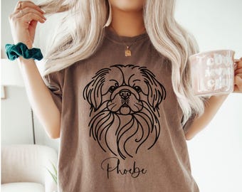 May include: A brown t-shirt with a black line drawing of a Pekingese dog and the name "Phoebe" printed on the front.