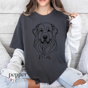 Op de afbeelding: Een donkergrijs T-shirt met een zwarte lijntekening van een hondenkop. De naam van de hond, "Max", staat onder de tekening.