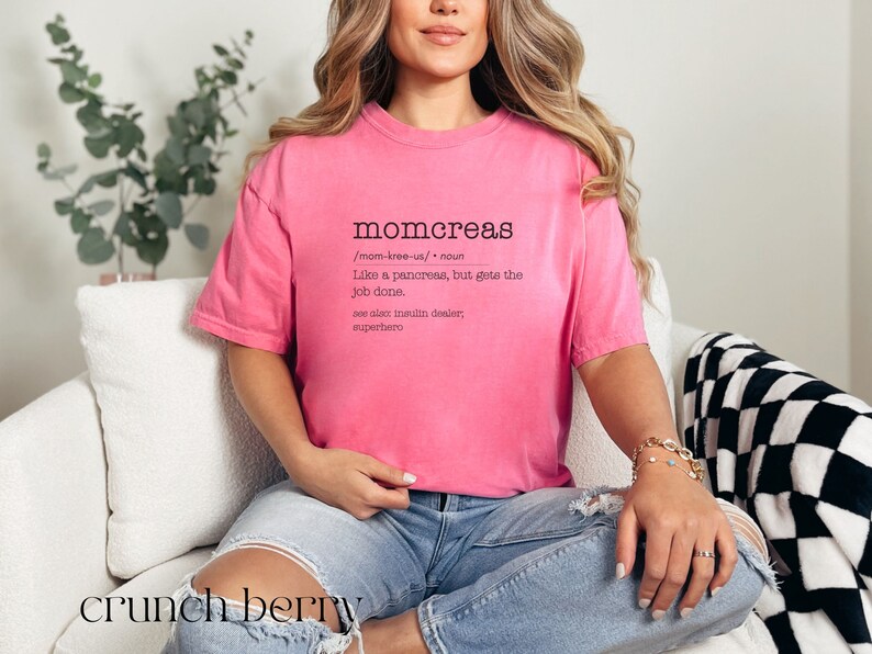 May include: A pink t-shirt with a humorous definition of "momcreas" printed on the front. The definition reads: "Like a pancreas, but gets the job done. See also insulin dealer, superhero."