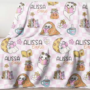 May include: A pink and white checkered blanket featuring a repeating pattern of cartoon ghosts reading books, flowers, coffee cups, and pumpkins. The name "ALISSA Lane" is also printed on the blanket.