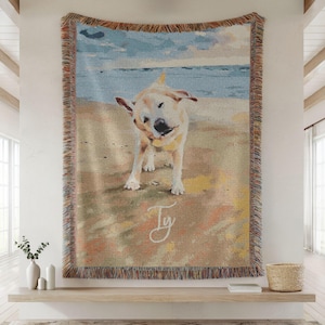 May include: Woven tapestry throw blanket featuring a golden Labrador shaking its head on a beach. The artwork has a watercolor style with a blue sky and ocean background. The blanket has a fringed border and the name "Ty" is written in cursive.
