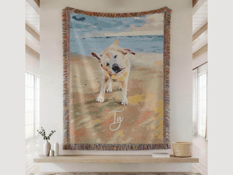 May include: Woven tapestry throw blanket featuring a golden Labrador shaking its head on a beach. The artwork has a watercolor style with a blue sky and ocean background. The blanket has a fringed border and the name "Ty" is written in cursive.