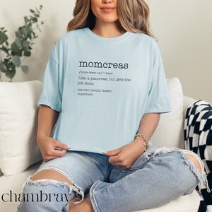 May include: A light blue t-shirt with the word "momcreas" defined as "Like a pancreas, but gets the job done." The text is in black and the shirt is on a person sitting on a white couch.