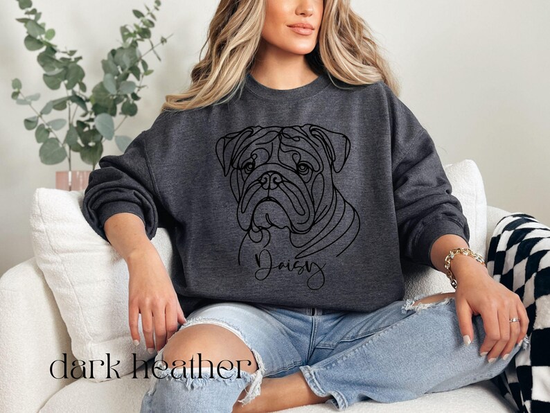 K&ouml;nnte beinhalten: Dunkelgraues Sweatshirt mit einer Strichzeichnung eines Bulldoggen-Gesichts und dem Namen "Daisy" darunter. Der Text "dark heather" ist unten aufgedruckt. Ein l&auml;ssiger, bequemer Stil.