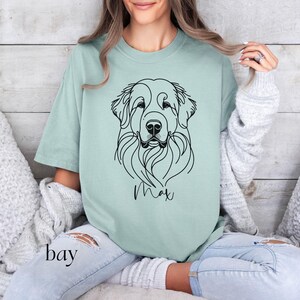 Op de afbeelding: Een lichtgroen T-shirt met een zwarte lijntekening van een hondenkop. De naam van de hond, "Max", staat onder de tekening.