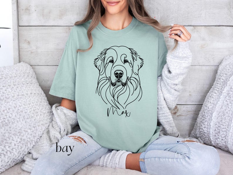 Op de afbeelding: Een lichtgroen T-shirt met een zwarte lijntekening van een hondenkop. De naam van de hond, "Max", staat onder de tekening.
