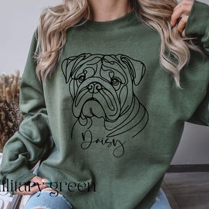 K&ouml;nnte beinhalten: Milit&auml;rgr&uuml;nes Sweatshirt mit einer schwarzen Strichzeichnung eines Bulldoggen-Gesichts und dem Namen "Daisy" in Schreibschrift. Der Text "military green" ist unten aufgedruckt. Das Sweatshirt ist einfarbig.