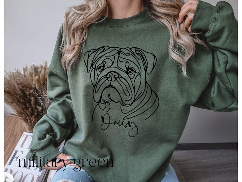 K&ouml;nnte beinhalten: Milit&auml;rgr&uuml;nes Sweatshirt mit einer schwarzen Strichzeichnung eines Bulldoggen-Gesichts und dem Namen "Daisy" in Schreibschrift. Der Text "military green" ist unten aufgedruckt. Das Sweatshirt ist einfarbig.