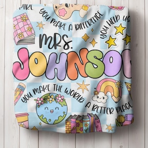 May include: A blue and white checkered fabric with the text "You make a difference" and "You help us". The text "Mrs. Johnson" is in large, colorful letters. The fabric also features a rainbow, a globe, and a stack of books.