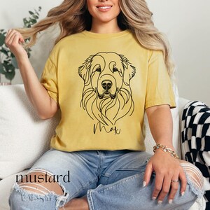 Op de afbeelding: Een geel T-shirt met een lijntekening van een hondenkop en de naam "Max" erop gedrukt.