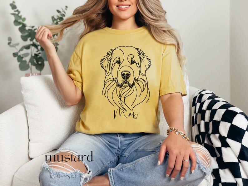 Op de afbeelding: Een geel T-shirt met een lijntekening van een hondenkop en de naam "Max" erop gedrukt.