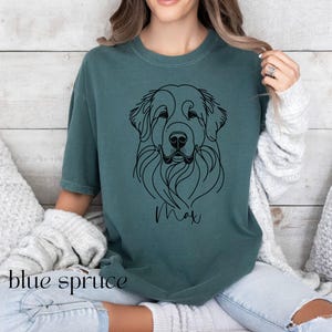 Op de afbeelding: Een tealblauw t-shirt met een zwarte lijntekening van een hondenkop. De naam van de hond, "Max", staat onder de tekening.