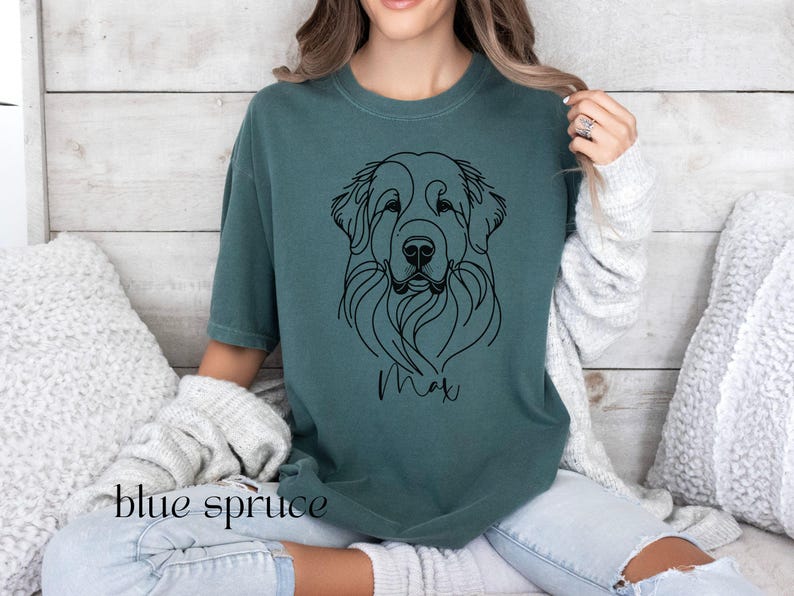 Op de afbeelding: Een tealblauw t-shirt met een zwarte lijntekening van een hondenkop. De naam van de hond, "Max", staat onder de tekening.