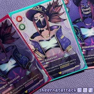 May include: Three rectangular trading cards featuring an illustration of a character named Akali, the Rogue Assassin. The character wears a black cap, a face mask, and a purple jacket. The cards include game text and icons in purple, red, and green.