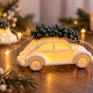 May include: A white ceramic car figurine illuminated from within, featuring a textured green pine tree secured to its roof. The car is surrounded by thin, glowing string lights and positioned near evergreen branches and white berries.