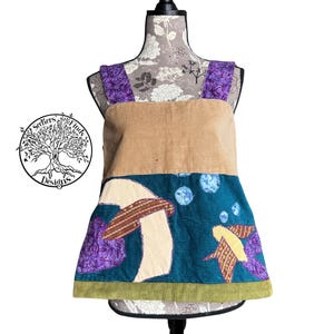 May include: A corduroy top with a unique design. The top features a tan upper section and a teal lower section with embroidered mushroom and fish motifs. Purple straps and a green hem add color. The top is displayed on a mannequin.