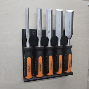 May include: A set of six chrome vanadium chisels with black and orange handles, mounted on a black wall-mounted holder. The chisels are labeled with their sizes: 1/2", 1/4", 1/8", 1/16", 1/32", and 1/64".