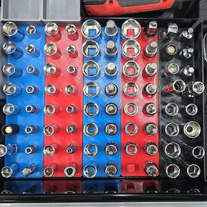 May include: A tool organizer with various sockets arranged in rows. The organizer is divided into red and blue sections, providing a structured layout for different socket sizes. The sockets are made of metal and are designed for use with a wrench or ratchet.