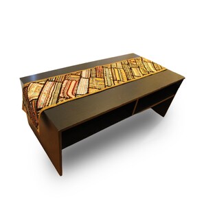 May include: A dark brown coffee table with a colourful, patterned table runner. The runner features a patchwork design with various colours including red, yellow, and brown. The table has a rectangular shape with two open shelves.