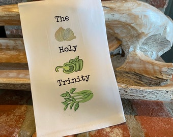 May include: White kitchen towel with the text "The Holy Trinity" and illustrations of an onion, green pepper, and celery.