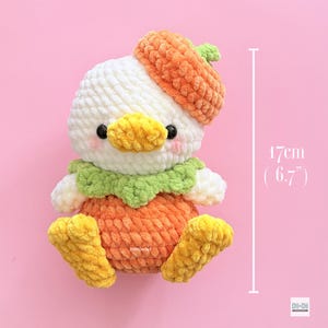 May include: A white crocheted plush duckling wearing an orange hat and orange body, featuring a green collar, yellow beak, and yellow feet. The plush toy measures 6.7 inches in height. It has black eyes and pink blush marks on its cheeks.
