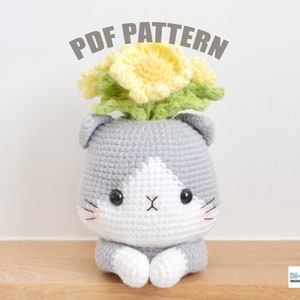 Könnte beinhalten: Häkelmuster für einen grauen und weißen Katzentopf mit gelben Blumen oben. Das Muster heißt "PDF PATTERN".