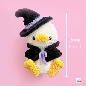 May include: A white crocheted duck plushie wearing a black witch hat with a lavender band and a matching black cape with lavender ties. The duck has yellow feet and a yellow beak, measuring 7.8 inches in height as indicated by the text.