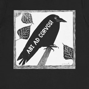 May include: Black t-shirt featuring a black and white graphic of a crow perched on a branch, with the text "ABI AD CORVOS!". The design includes stylized leaves in the background, creating a nature-inspired theme.