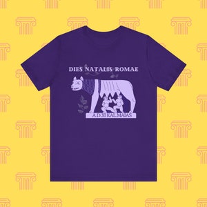 May include: Purple t-shirt with a graphic of the she-wolf and the twins, a symbol of Rome. The text on the shirt reads "Dies Natalis Romae" and "A.D.XI Kal.Maias".