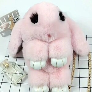 May include: A pink fluffy bunny shaped purse with a gold chain strap. The purse has black eyes and white paws.