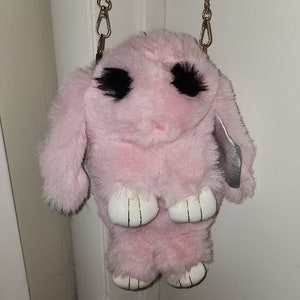 May include: A pink plush bunny bag with black eyes and white paws. The bag has a gold chain strap.