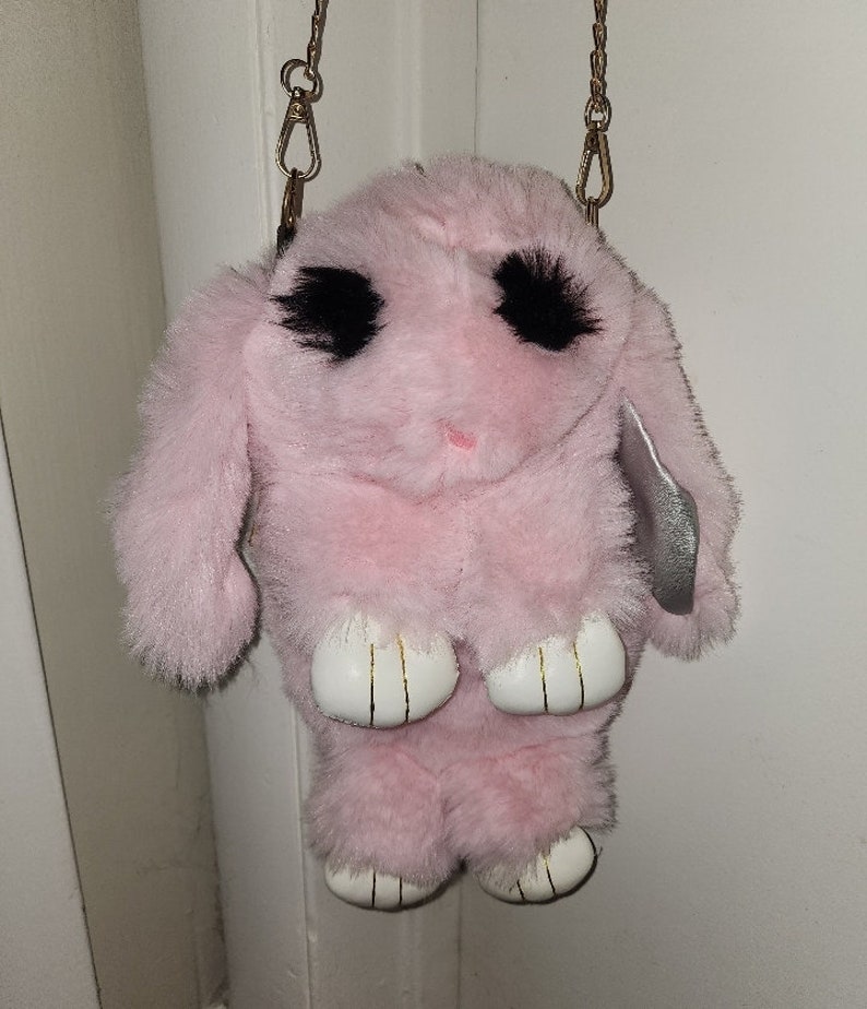 May include: A pink plush bunny bag with black eyes and white paws. The bag has a gold chain strap.
