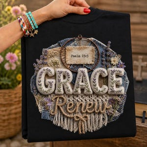 Könnte beinhalten: Ein schwarzes Sweatshirt mit einem kreisförmigen Design, das das Wort GRACE in gestickten Buchstaben, das Wort Renew in Seil-Schrift und einen kleinen rechteckigen Aufnäher mit der Aufschrift Psalm 23:3 zeigt. Es enthält Trockenblumen, Denim und Makramee-Fransen.
