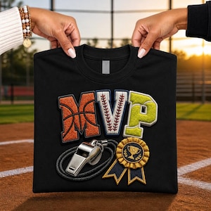 May include: A black t-shirt featuring the letters MVP in a sports-themed design. The M resembles a basketball, the V a baseball, and the P a tennis ball. Below the letters is a silver metal whistle with a black cord and a gold award ribbon.