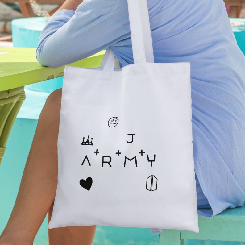May include: White tote bag with black text and symbols. The text reads "J ARMY" with a crown, a heart, a smiley face, and a symbol that looks like a butterfly.