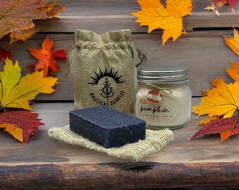 May include: A dark blue bar of soap on a natural fiber soap saver, a small burlap bag with a nautical logo, and a jar candle with a "Hello Pumpkin" label. Autumn leaves in shades of red, orange, and yellow surround the items.