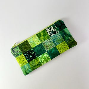 May include: A rectangular zipped pouch featuring a patchwork design of various green fabric squares. The exterior displays a mix of shades including lime, emerald, and forest green with diverse patterns such as stars, florals, and textures.