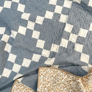 Op de afbeelding: Een blauw en wit geruit dekbed met een bloemenpatroon aan de achterkant. Het dekbed is gemaakt van katoen en perfect voor een knusse en comfortabele nachtrust.