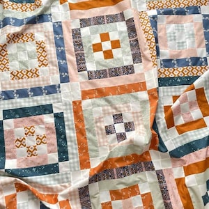 May include: A quilt made from a variety of fabrics in shades of orange, pink, white, blue and green. The quilt is made up of squares and rectangles, and the fabric patterns include gingham, floral and geometric designs.