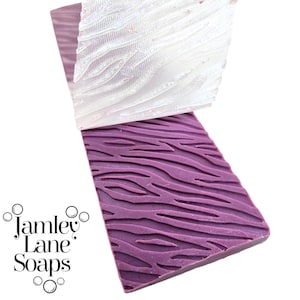 May include: Rectangular purple soap with a zebra stripe pattern, with a white soap on top with a similar pattern. The soap is from Jamley Lane Soaps.