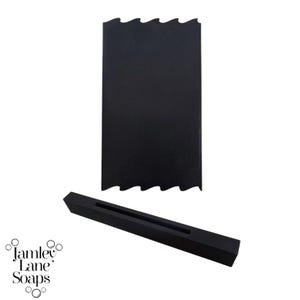 Puede incluir: Molde de jabón de silicona negro con un borde superior ondulado y una base rectangular. El molde está diseñado para crear una barra de jabón con una parte superior ondulada.