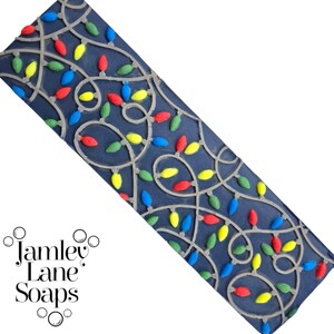 May include: A dark blue rectangular soap mold featuring a string of colorful Christmas lights. The lights are red, yellow, green, and blue. The mold is made of a flexible material, and the design is raised. The brand name "Jamley Lane Soaps" is in the lower left corner.