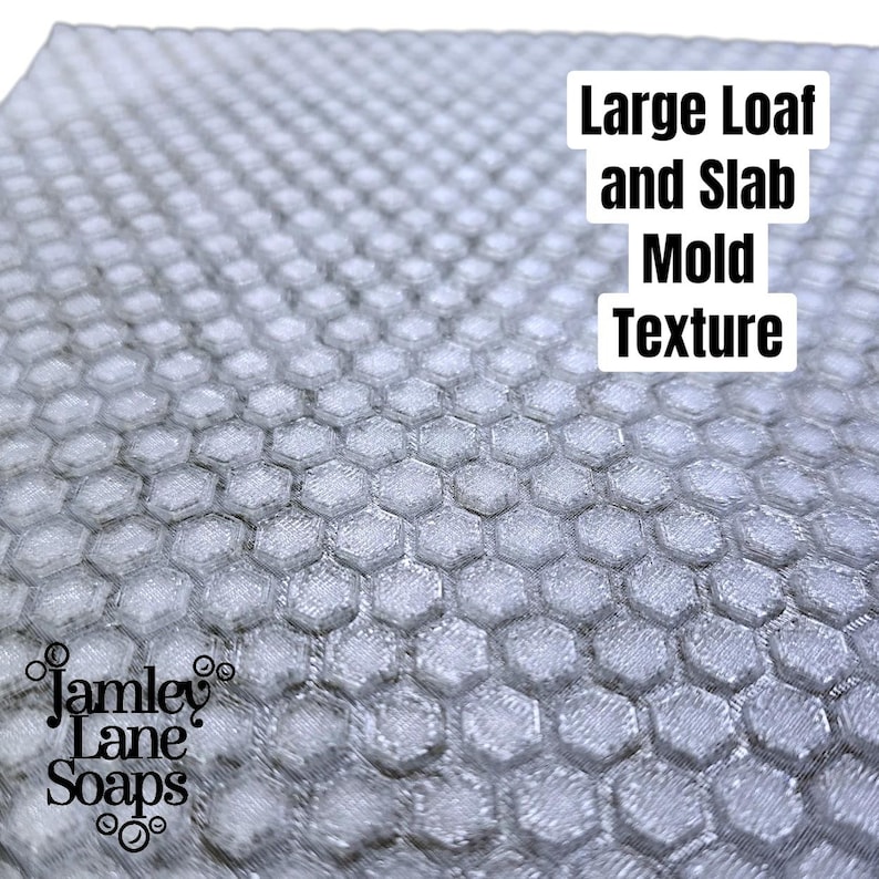 May include: A close-up of a grey honeycomb-patterned mold. The mold has a textured surface and is designed for large loaf and slab soap making. The text "Large Loaf and Slab Mold Texture" is visible. The Jamley Lane Soaps logo is in the lower left corner.