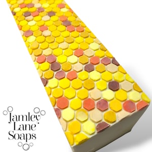 Puede incluir: Una pastilla de jabón con un patrón de panal en tonos amarillos, naranjas y morados. El jabón está hecho por Jamley Lane Soaps.