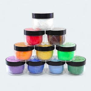 May include: A set of ten small glass jars with black lids, each filled with a different colored substance. The jars are arranged in a pyramid shape, with the white jar at the top.