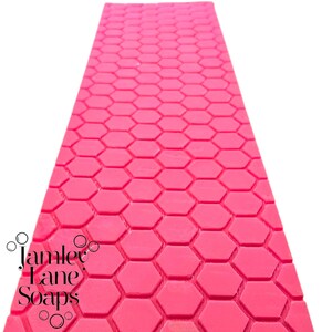 May include: A pink mold with a honeycomb pattern. The mold is designed for making soap, candles, or other crafts. The mold is made by Jamlee Jane Soaps.