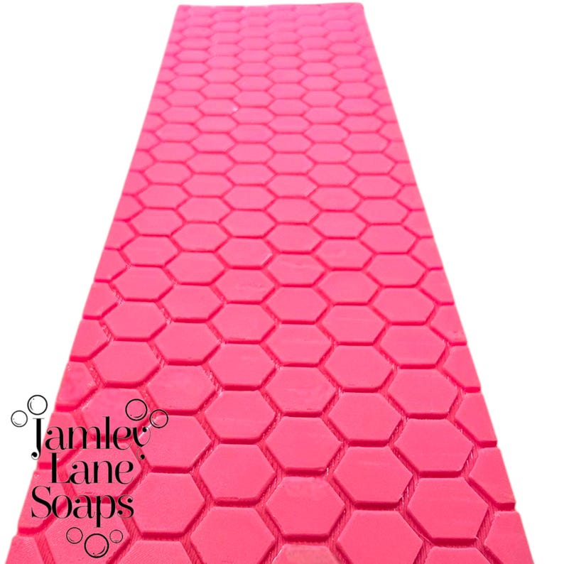 May include: A pink mold with a honeycomb pattern. The mold is designed for making soap, candles, or other crafts. The mold is made by Jamlee Jane Soaps.