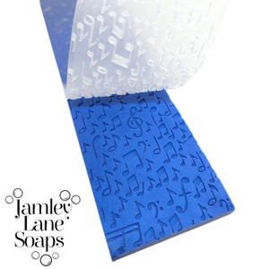 May include: A blue soap mold with a musical note pattern is partially peeled back to reveal a clear, embossed sheet with the same design. The logo "Jamley Lane Soaps" is visible in the lower left corner. The soap mold is a vibrant blue.