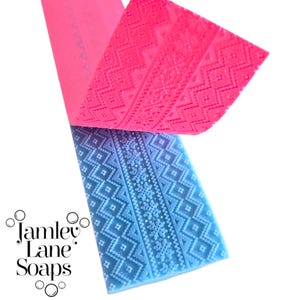Könnte beinhalten: Zwei Seifenformen, eine rosa und eine blaue, mit einem detaillierten geometrischen und Schneeflockenmuster. Die rosa Form ist teilweise abgezogen und gibt die blaue Form darunter frei. Der Markenname "Jamley Lane Soaps" ist unten links sichtbar.