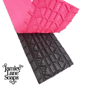 May include: A rectangular silicone mold with a detailed tire tread pattern, shown with a bright pink cast piece being lifted from the dark gray mold. The logo for Jamley Lane Soaps is printed in black text in the lower left corner of the image.
